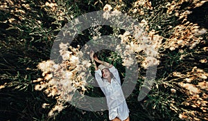 Pretty young woman is lying among the flowers and grass on meadow