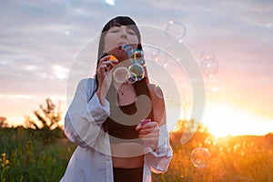 pretty young woman making soap bubbles in summer green field on sunset. happy peaceful time. millennial generation