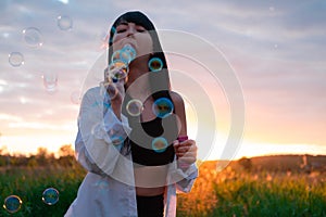 pretty young woman making soap bubbles in summer green field on sunset. happy peaceful time. millennial generation