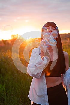 pretty young woman making soap bubbles in summer green field on sunset. happy peaceful time. millennial generation