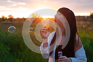 pretty young woman making soap bubbles in summer green field on sunset. happy peaceful time. millennial generation