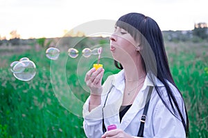 pretty young woman making soap bubbles in summer green field on sunset. happy peaceful time. millennial generation