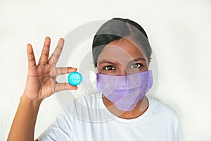 Pretty young woman with mask holding a container with contact lenses for eyesight. Wearing face mask