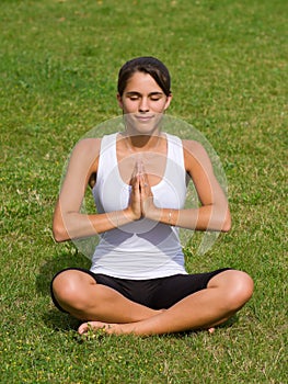 Pretty young woman meditating on grass