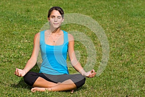 Pretty young woman meditating on grass