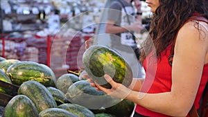 Pretty young woman or mother makes purchases in a supermarket, chooses food watermelon, avocado, fruits, carrots