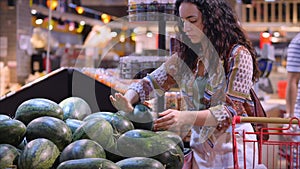 Pretty young woman or mother makes purchases in a supermarket, chooses food watermelon, avocado, fruits, carrots