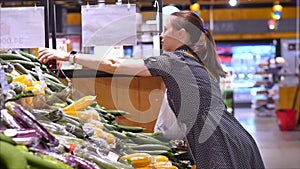 Pretty young woman or mother makes purchases in a supermarket, chooses food watermelon, avocado, fruits, carrots