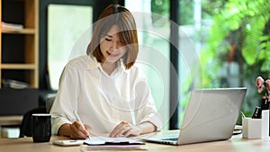 Pretty young woman office worker using laptop computer and preparing annual financial report at office desk