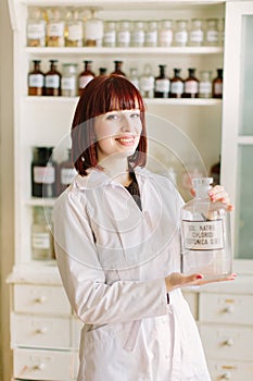 Pretty young woman pharmacist in assistance room holding bottle with isotonic solution