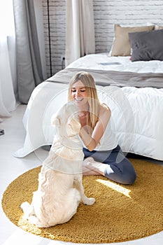 Pretty young woman playing with her dog while sitting on the floor at home