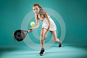 Pretty young woman playing padel indoor over green-blue background. photo