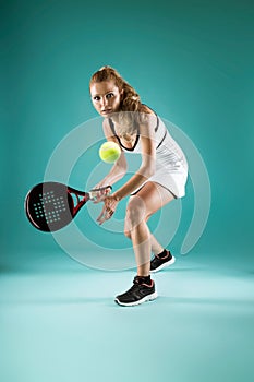 Pretty young woman playing padel indoor over green-blue background.