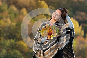 Pretty young woman in a poncho with autumn leaves in hands. Girl touched the hair. Portrait