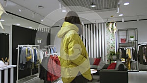 Pretty young woman is posing dressed in a yellow jacket at clothing store, tracking shot, 360 degree