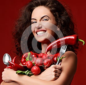 Pretty young woman posing with fresh red vegetables radish chili pepper green leaves lettuce parsley smiling