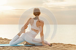 Pretty young woman practicing yoga at the beach on sunrise. Fit girl doing stretching exercise on see background