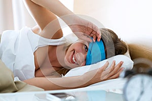 Pretty young woman pulling up sleeping mask and looking at camera after wake up in the bedroom at home.