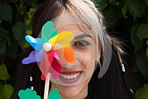 Pretty young woman in punk style holds a colourful windmill in her hand. She is looking at the camera smiling. Summer, air