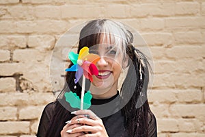 Pretty young woman in punk style holds a colourful windmill in her hand. She is looking at the camera smiling. Summer, air