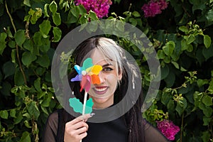 Pretty young woman in punk style holds a colourful windmill in her hand. She is looking at the camera smiling. Summer, air