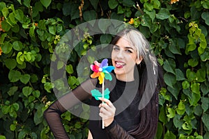 Pretty young woman in punk style holds a colourful windmill in her hand. She is looking at the camera smiling. Summer, air