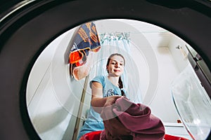 Pretty young woman putting dirty clothes into a washing machine. View from inside of washer machine. Washing clothes at home,