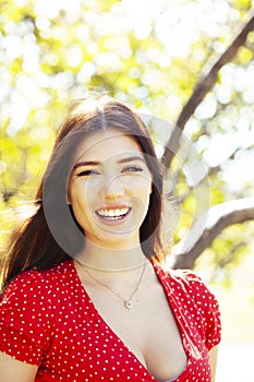 Pretty young woman in red dress smiling cheerful in green park at tree on summer sunny day, lifestyle people concept