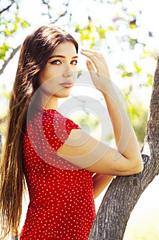 Pretty young woman in red dress smiling cheerful in green park at tree on summer sunny day, lifestyle people concept