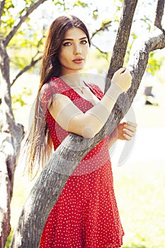 Pretty young woman in red dress smiling cheerful in green park at tree on summer sunny day, lifestyle people concept