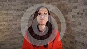 A pretty young woman in a red hoodie with long hair resents, expresses her negative emotions and waves her hands on a