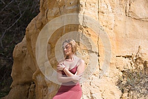 pretty young woman in red summer dress is posing on the cliff. The woman makes different body expressions. In the background rocks