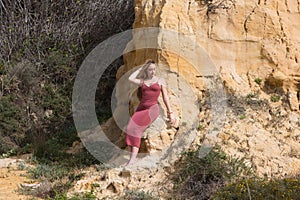 pretty young woman in red summer dress is posing on the cliff. The woman makes different body expressions. In the background rocks
