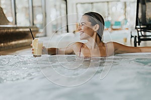 Young woman relaxing in the indoor swimming pool with glass of fresh orange juice