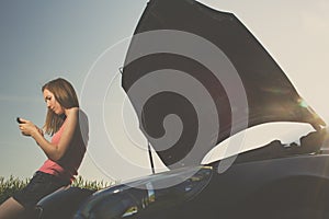 Pretty, young woman by the roadside after her car has broken down