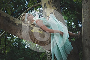 Pretty young woman in romantic dress lie on tree summer day