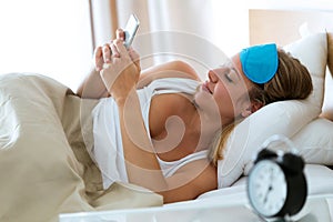 Pretty young woman sending text message with her smartphone after wake up in the bedroom at home.