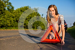 Pretty, young woman setting the safety triangle on the roadside