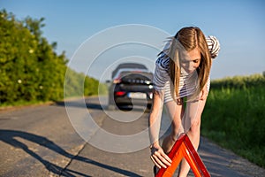 Pretty, young woman setting the safety triangle on the roadside