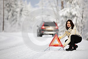 Pretty, young woman setting up a warning triangle and calling for assistance after her car broke down