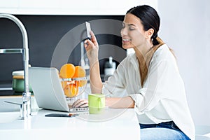 Pretty young woman shopping online with credit card while staying in the kitchen at home