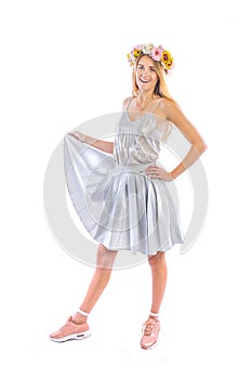 A pretty young woman in a silver pleated skirt holds the edge of the skirt with one hand, in pink sneakers and a