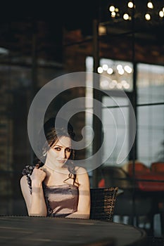 Pretty young woman sitting in outdoor cafe in front of glass windows
