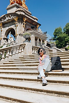 Pretty young woman sitting on the staircase in front of the fountain