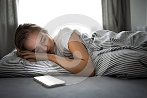 Pretty, young woman sleeping in her bed with her cell phone close to her.