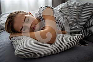 Pretty, young woman sleeping in her bed with her cell phone close to her.