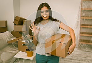 Pretty young woman standing with cardboard box in her hand showing ok with her fingers.