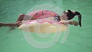 Pretty young woman in sunglasses enjoys the sun swimming in the pool lying on pink rubber ring. Leisure of lonely lady