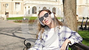 Pretty young woman in sunglasses and headphones listening to music, singing and dancing outdoors