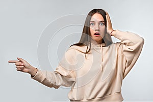Pretty young woman surprised and pointing finger to the side, shows copy space for your information